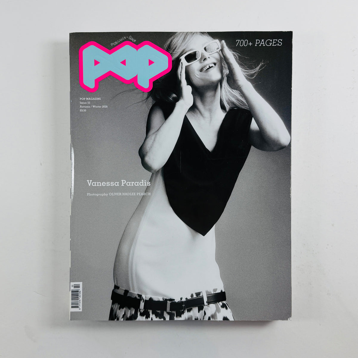 A single magazine lying flat on a light neutral background. The cover is predominantly black-and-white with a large bright pink and blue 'POP' masthead at the top left, plus visible text including 'Vanessa Paradis' and '700+ PAGES'.