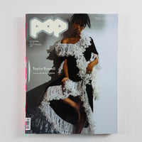 A magazine titled 'POP' lying flat on a light gray surface. The cover features a fashion photograph of a woman wearing a black dress with dramatic white feathered or fringed trim, and the cover text includes 'Taylor Russell' and '700+ PAGES'.